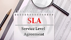 Desktop magnifier, reports, pen and notebook with text SLA Service Level Agreement. Business concept