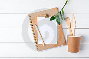 Desktop mockup planner. Flat lay of white wooden table background. Top view green sprout leaves, coffee cup, cutlery, blank, craft