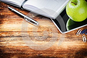 Desktop with paper agenda, digital tablet and green apple