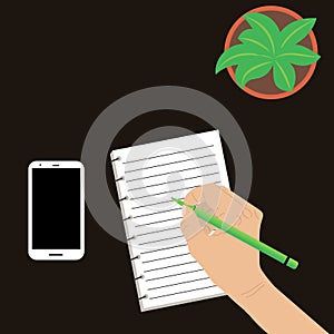 Desktop with a plant green. Holds a ballpoint pen female hand. Notepad with lines and a smartphone.