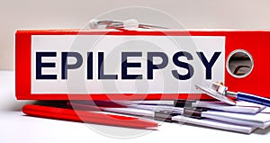 On the desktop is a stethoscope, documents, a pen, and a red file folder with the text EPILEPCY. Medical concept