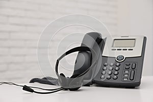 Desktop telephone and headset on white table in office, space for text. Hotline service