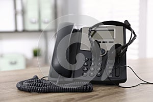 Desktop telephone and headset on wooden table in office. Hotline service