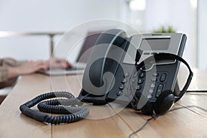 Desktop telephone with headset on wooden table in office. Hotline service