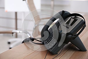 Desktop telephone and headset on wooden table in office, space for text. Hotline service