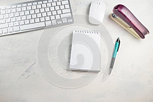 Desktop top view. Blank notepad with pen, keyboard, mouse and stapler on the desktop