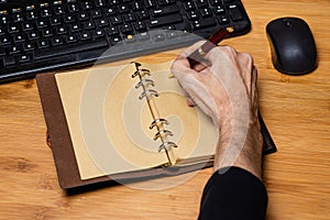 Desktop workspace with keyboard and mouse partially visible.  Vintage style notebook with a finely crafted wooden pen being used