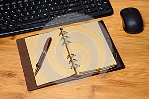 Desktop workspace with keyboard and mouse partially visible.  Vintage style notebook with a finely crafted wooden pen provides