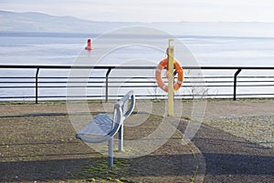 Desolate beach esplanade with empty seat bench and orange water safety buoy ring