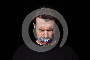 Conceptual portrait of young upset man with three colors duct tape over his mouth isolated on dark background