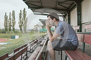Despair and depressed man is sitting on bench at stadium