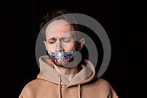 Close-up portrait of young emotive man with three colors duct tape over his mouth isolated on dark background