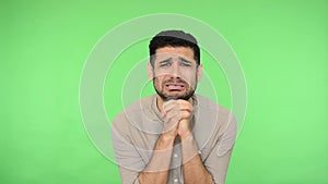 Despaired brunette man clasping hands in prayer, looking pleadingly almost cry. green background, chroma key