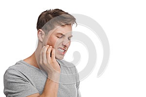 Despaired millennial caucasian attractive male presses his hand to cheek and suffers from toothache