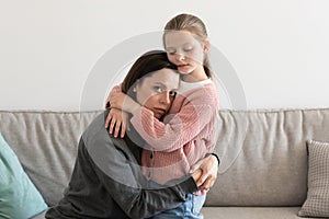 Despaired sad european millennial mom hugging little girl, daughter calms woman in living room