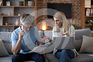Despaired sad mature caucasian couple work with documents and laptop, pay bills and taxes in living room