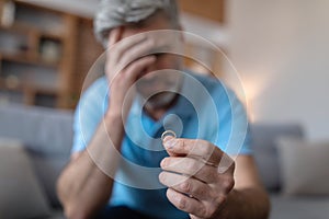 Despaired sad middle aged european man suffering from divorce, holds ring in hand, blurred, copy space