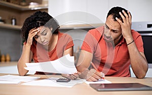 Despaired sad young african american lady and husband work with documents, pay taxes on kitchen interior