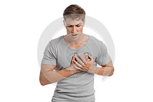 Despaired sad young european handsome guy presses his hands to sore spot and suffers from pain in chest