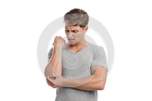 Despaired young european handsome guy presses his hand to sore spot and suffers from pain in elbow