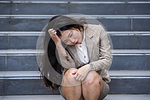 Desperate Asian American businesswoman crying alone sitting on street staircase suffering stress and depression crisis being