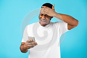 Desperate Black Man Holding Phone Reading Bad News, Blue Background