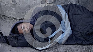 Desperate black man lying street covered with sleeping bag, poverty hopelessness