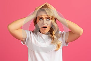 Desperate blonde woman touching head in frustration on pink background