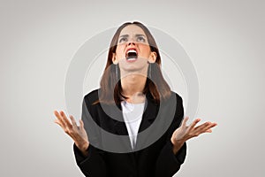 Desperate businesswoman in a black suit looking upwards with hands raised in exasperation