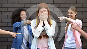 Desperate female teenager covering face by hands suffering school bullying