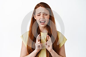 Desperate and hopeful redhead girl student praying, making wish with crossed fingers, sobbing and pleading god