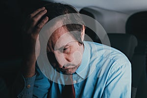 Desperate hopeless businessman at car back seat on his return from the work late at night, low key