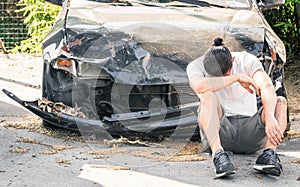Desperate man crying on his old damaged car after a crash