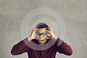 Portrait of scared desperate young black man holding his head and screaming in panic