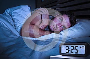 Desperate man in stress sleepless on bed with eyes wide opened suffering insomnia sleeping disorder depressed with digital alarm