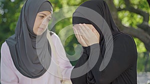 Desperate Muslim woman in hijab crying as friend calming her down. Portrait of young university student supporting