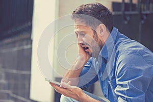 Desperate sad young man looking at bad text message on his mobile phone