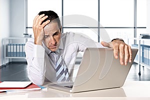 Desperate senior businessman in crisis working on computer laptop at office desk in stress under pressure