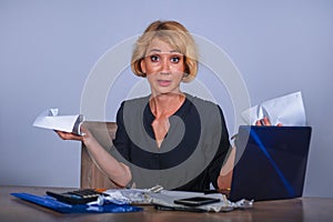 Desperate and stressed business woman working overwhelmed at office desk with laptop computer holding paperwork looking crazy and