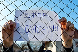 Desperate teenage boy wearing surgical mask holding a message  behind a wired fence in isolation