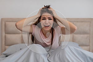Desperate woman in bed touching head, crying out in frustration