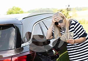 Desperate woman hold cash dollar bills next to car with an open tank, concept of rising fuel prices