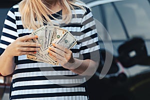 woman hold cash dollar bills next to car with an open tank, concept of rising fuel prices