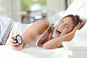 Desperate woman holding an alarm clock on the bed