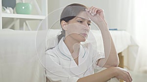 Desperate woman sitting on the floor in hospital ward and thinking. Portrait of stressed Caucasian doctor or nurse have