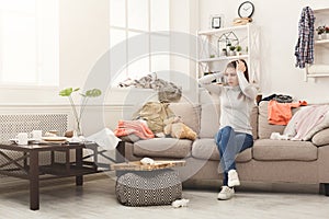 Desperate woman sitting on sofa in messy room