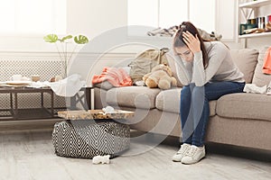 Desperate woman sitting on sofa in messy room