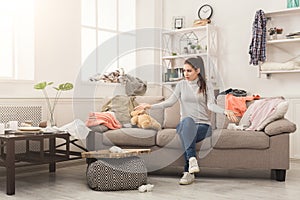 Desperate woman sitting on sofa in messy room