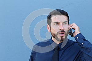 Desperate young brunette businessman get bad news heavy problems, faces challenges snort while talking on the mobile phone on blue photo