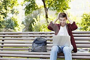 Desperate young man using laptop outdoors